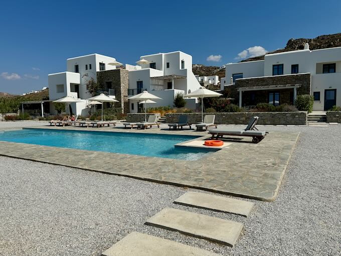 Concrete slabs leading to a blue pool in front of a Cycladic white hotel 