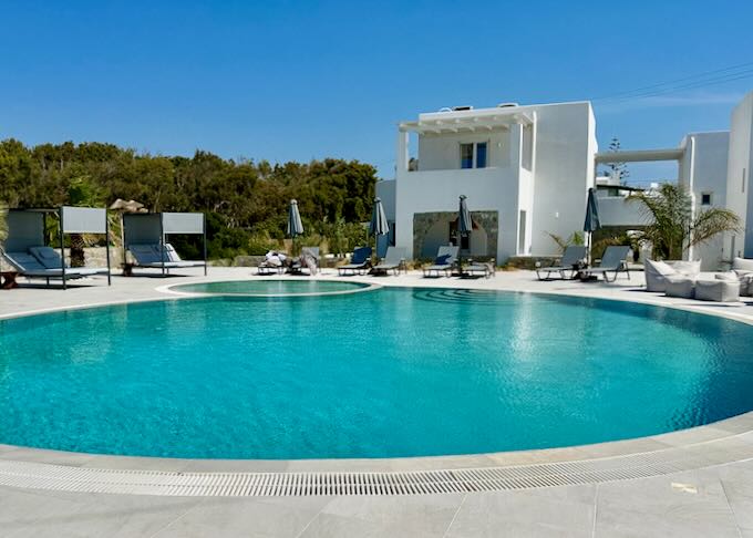 White Cycladic style hotel in back of a sparkling blue pool