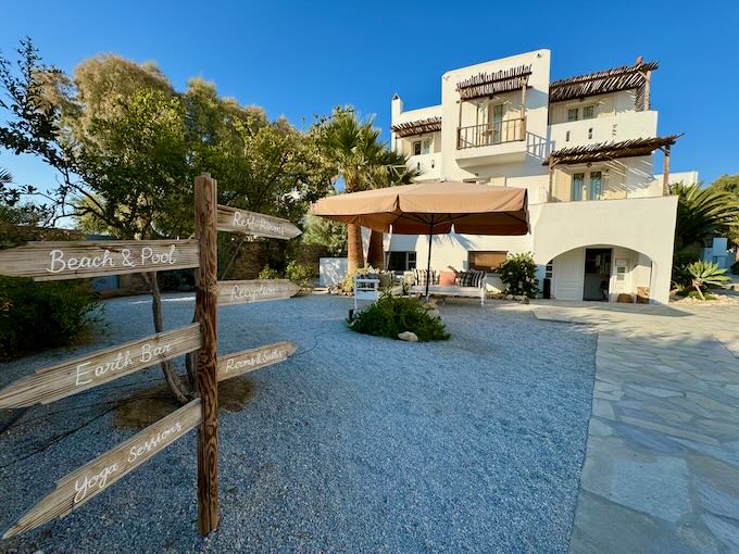 Cycladic-style hotel building with a signpost in front directing the way to the beach and yoga studio