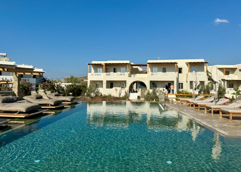 Large outdoor swimming pool backed by a white Cycladic style hotel