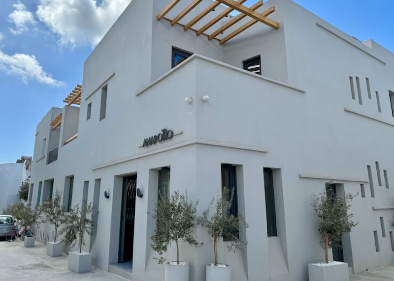 Sand-colored Cycladic-style hotel on a city street corner on a sunny day