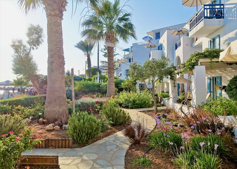 Path winding through lush gardens past a white Cycladic-style hotel.