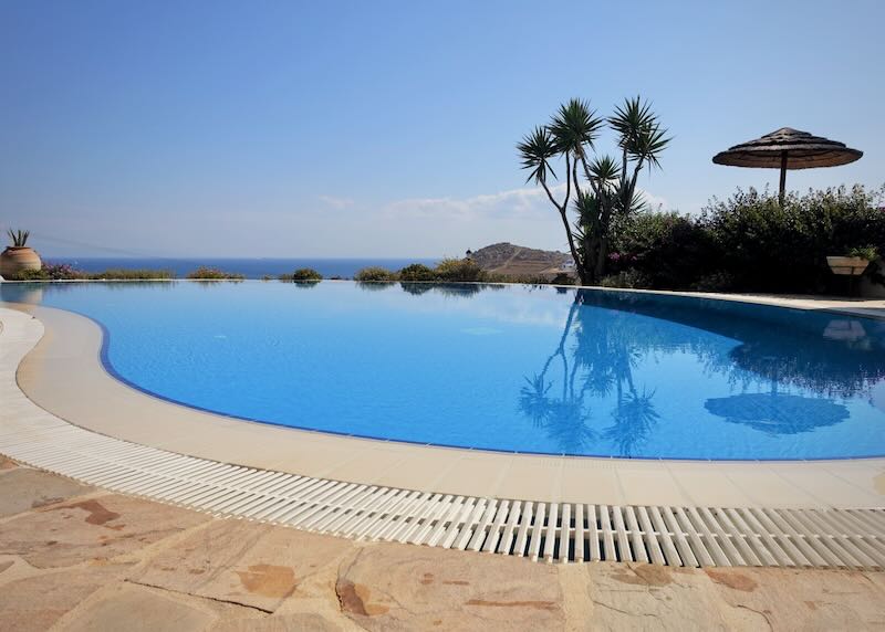 View of an infinity-style swimming pool overlooking a blue sea.