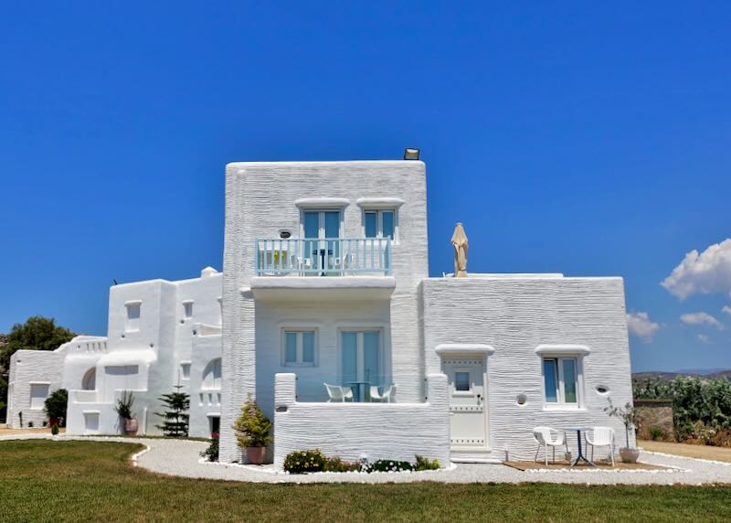 White cycladic-style hotel on a green lawn, against a blue sky