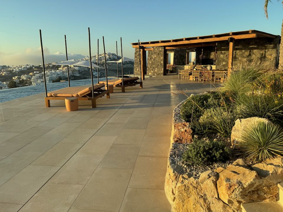 View over an expansive pool deck with an outdoor kitchen to the Greek village of Pyrgos on Santorini.