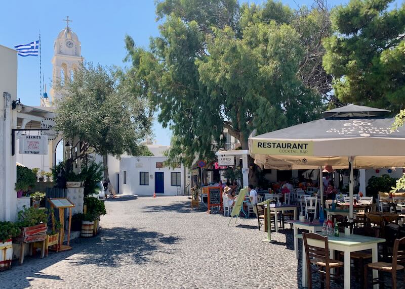 Greek village square with a church and outdoor cafe.