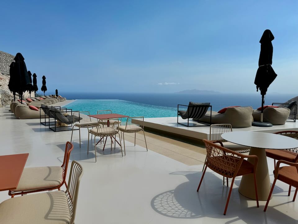 Hotel swim terrace with sun loungers and cafe tables, overlooking the blue sea.