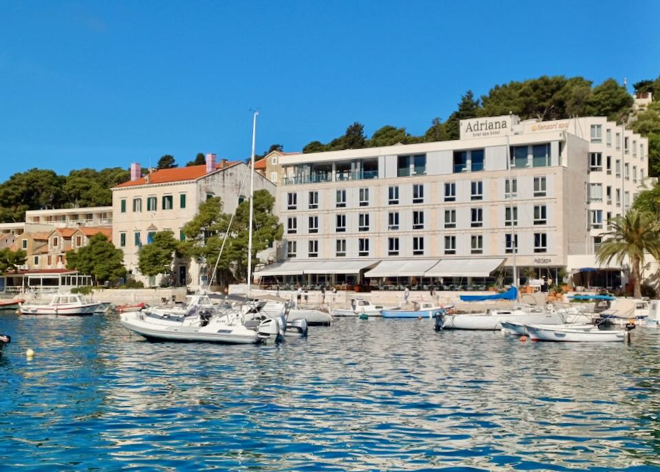 A multi-story building sits by a small harbor with several anchored boats.