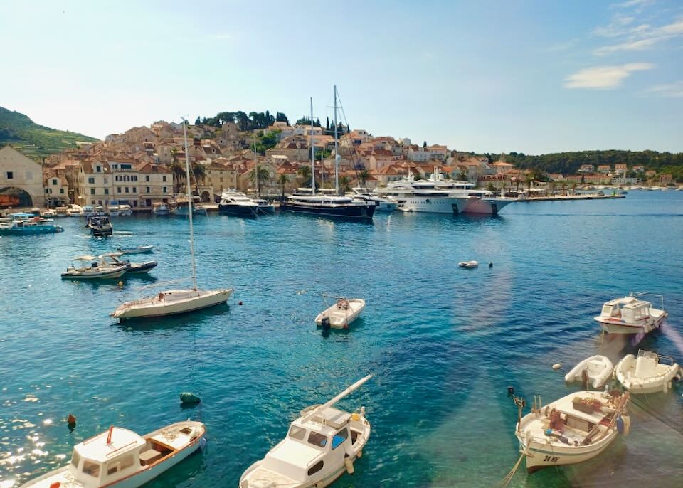 Boats sit in a blue harbor with a small town on a hill.