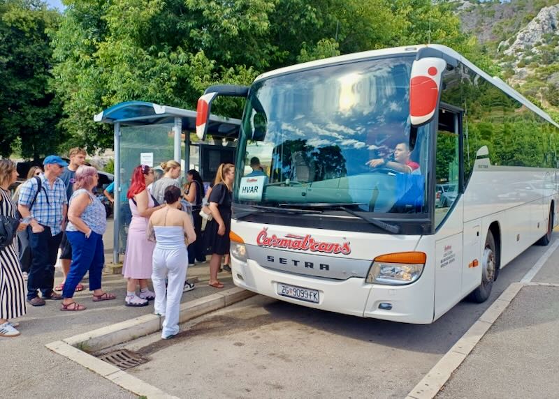 A bus driver points to a crowd of people loading a bus.