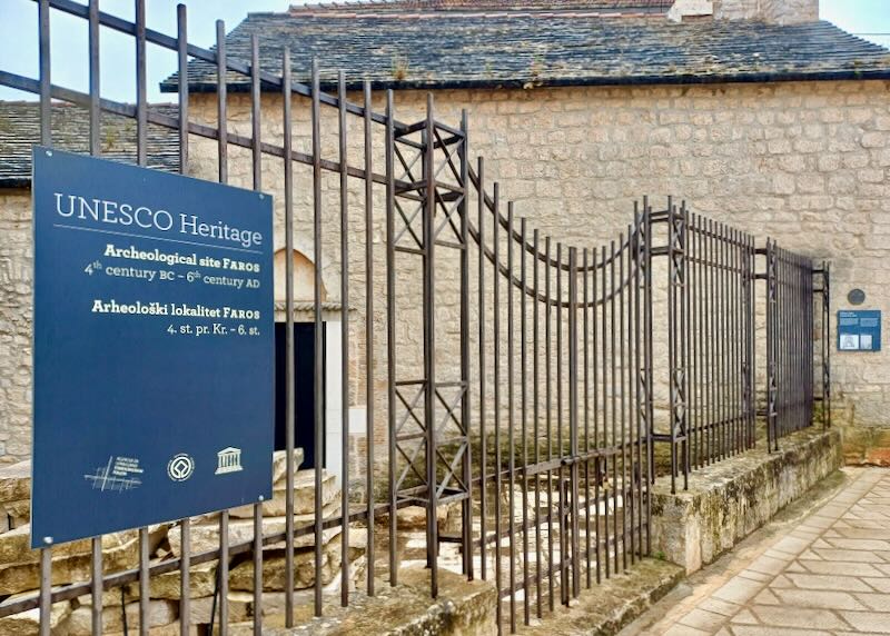 A navy-blue sign on a wrought iron gate states it's a UNESCO-Heritage Site.