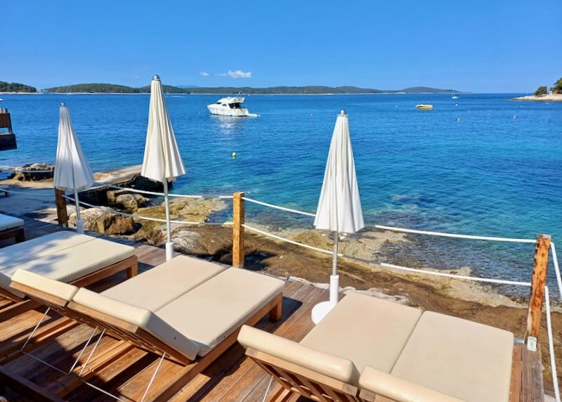 Tan cushioned lounge chairs sit by the water.