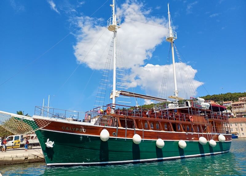 An old sailboat made of wood and painted dark green docks on shore.