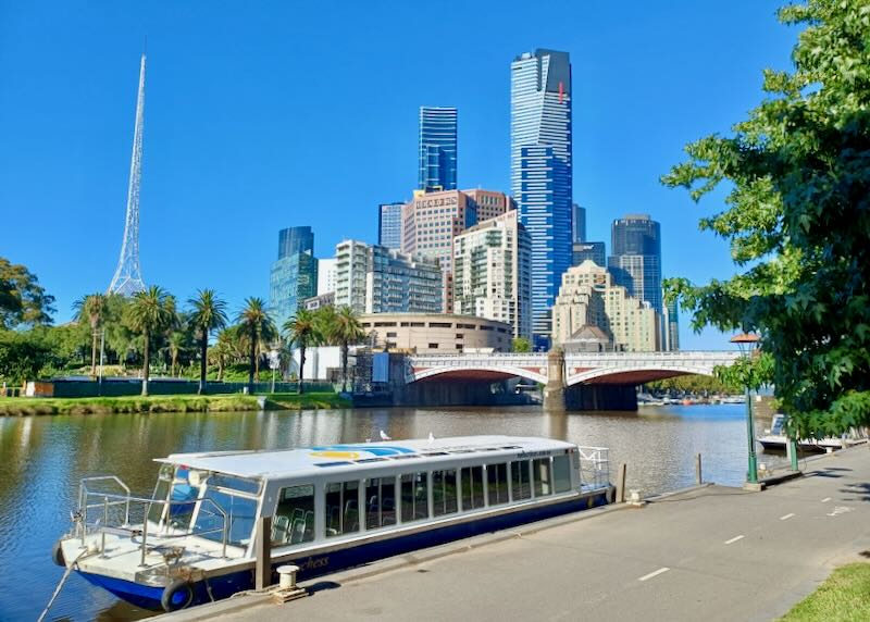 A tied up tourist boat along a river has a bridge and tall buildings in the background.