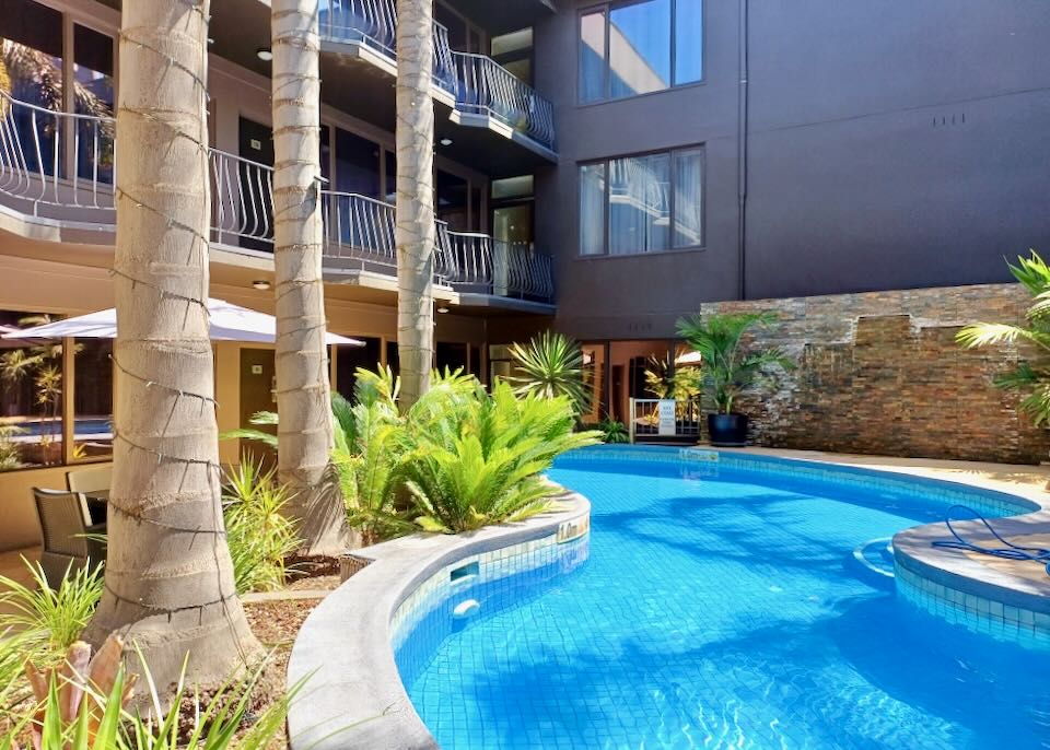 A blue pool meanders outside a hotel.