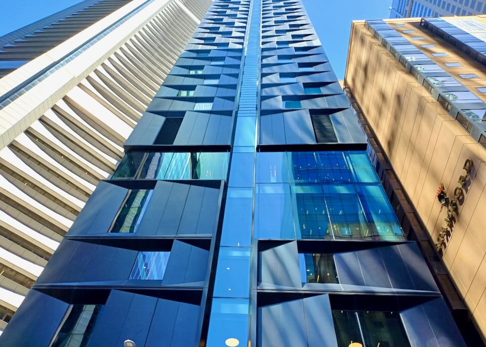 A tall thin building rises up from the ground with black and blue glass.