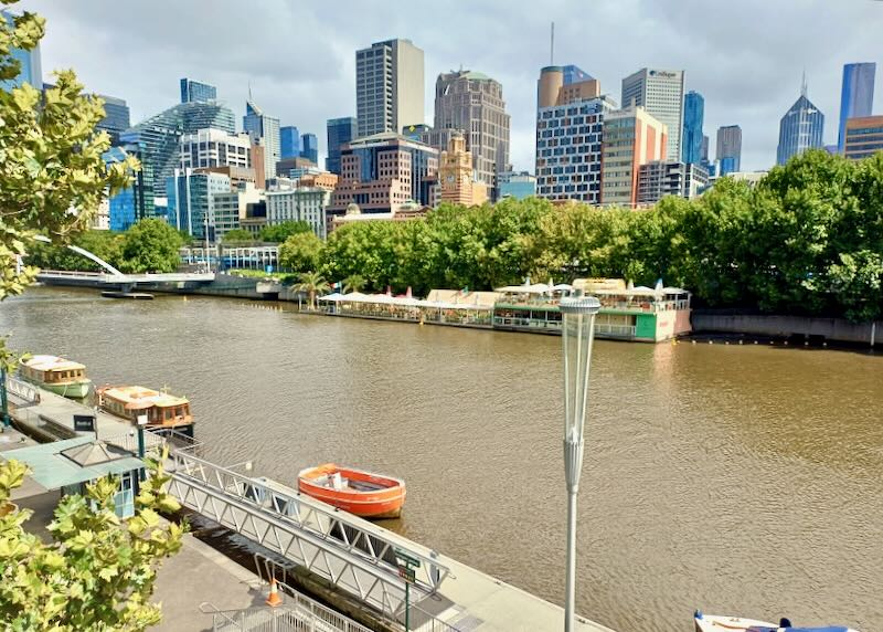 A brown river flows between two side and one side has tall buildings.