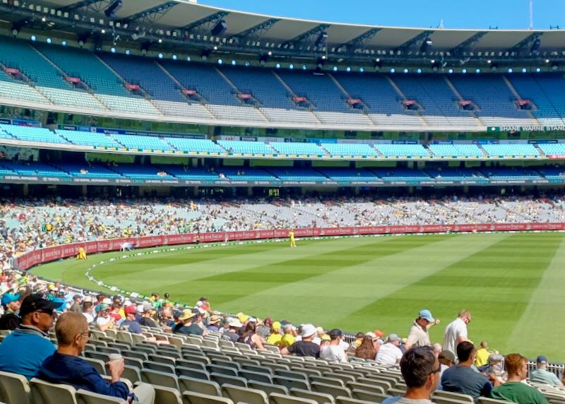 People sit in a large round outdoor stadium to watch cricket.