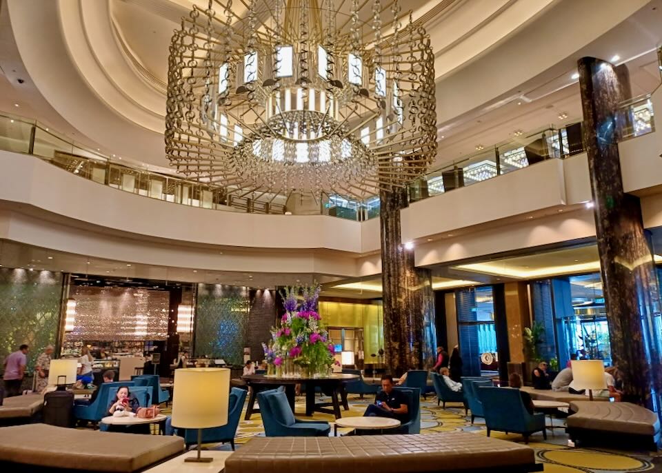 A large chandelier hangs over a lobby filled with blue velvet chairs and gold benches.