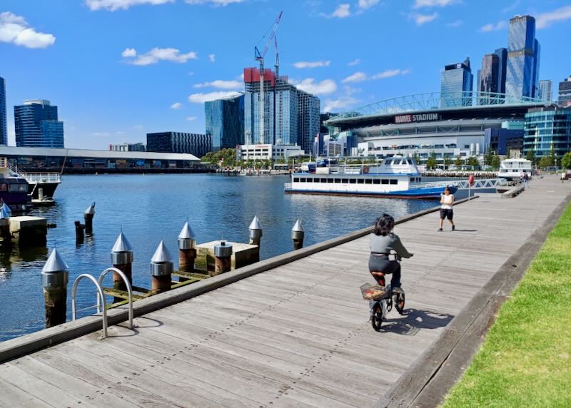 A woman rides her bike on a wood dock next to the river.