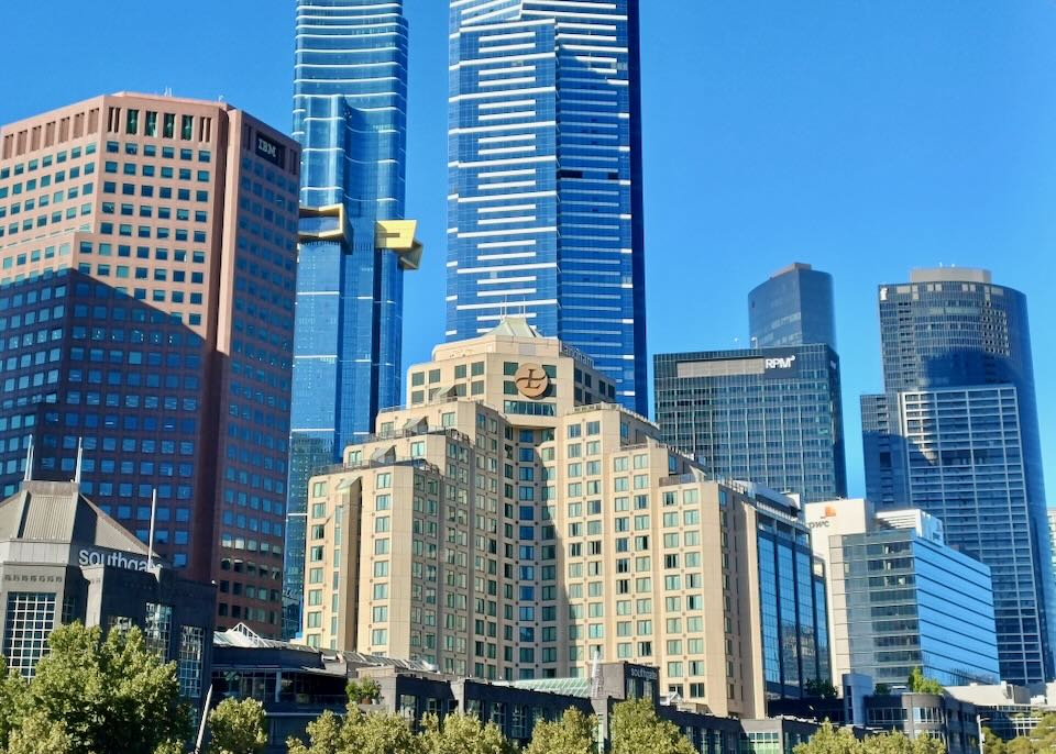 A tan-colored tall hotel sits in front of tall blue skyscrapers.