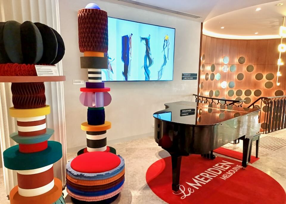 Tall colorful sculptures sit in a hotel lobby next to a black grand piano.