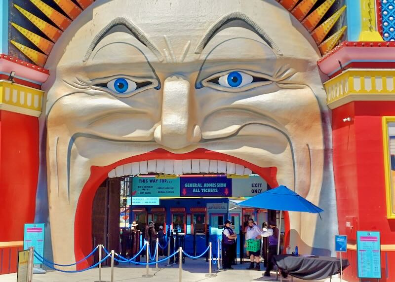 A large sculpture of a face covers the entrance to an amusement park, its open mouth provides an arch at the doors.