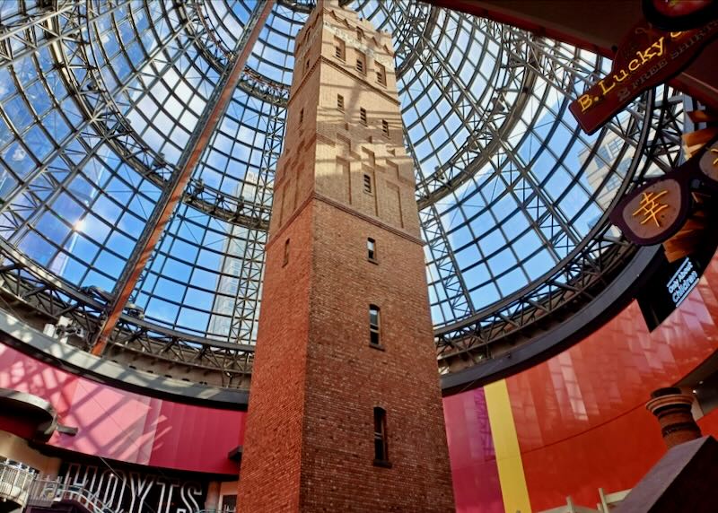 An old red brick tall building sits inside a glassed-in structure.