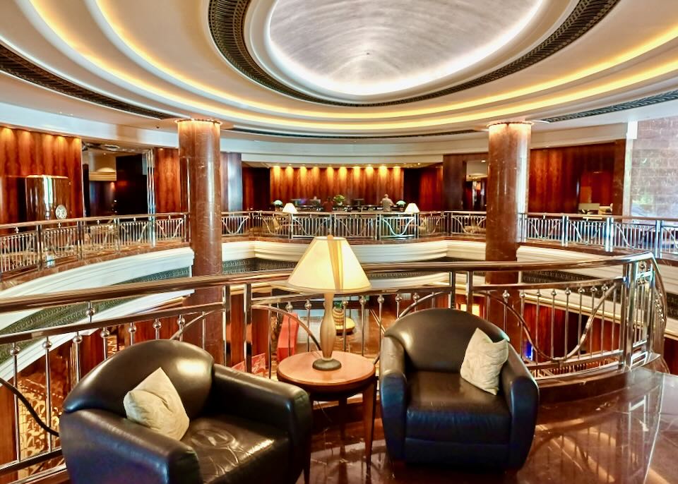 A hotel lobby on the second floor with ornate metal railings and large marble pillars.