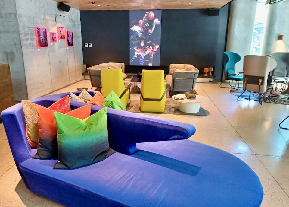 A purple lounge chair with orange, green, and red pillows sits in a hotel lobby.