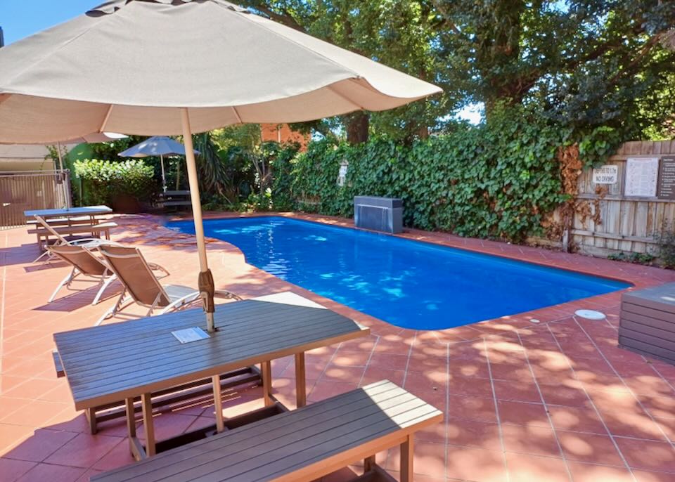 A medium-sized pool sits under trees and is surrounded by orange tile.