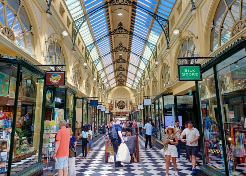 People shop in a domed glass-topped hall with ornate black metal buttresses.