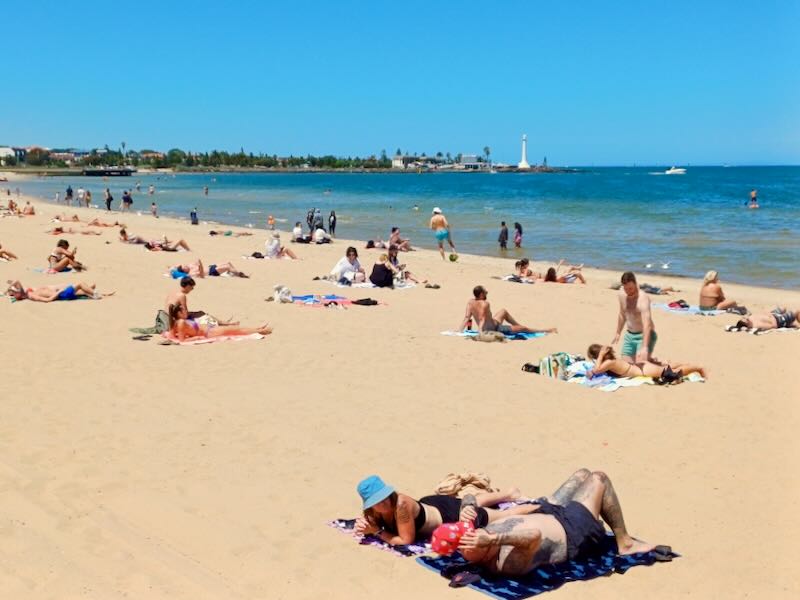 People lay on the beach by a blue sea.