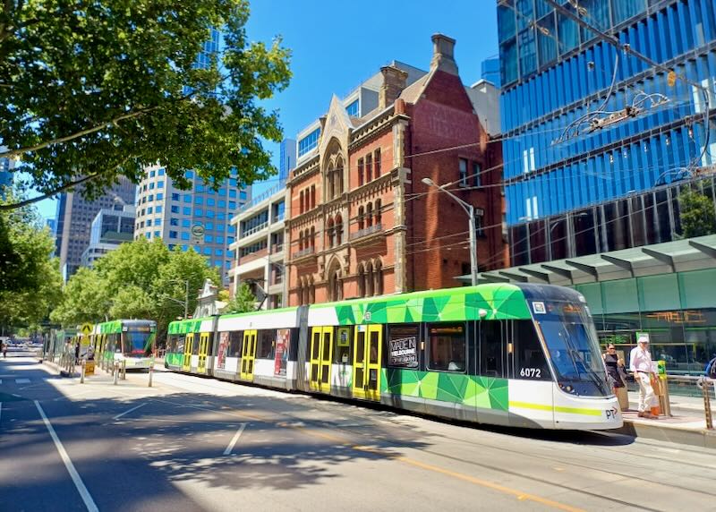 A long tram pulls into a stop along a street.