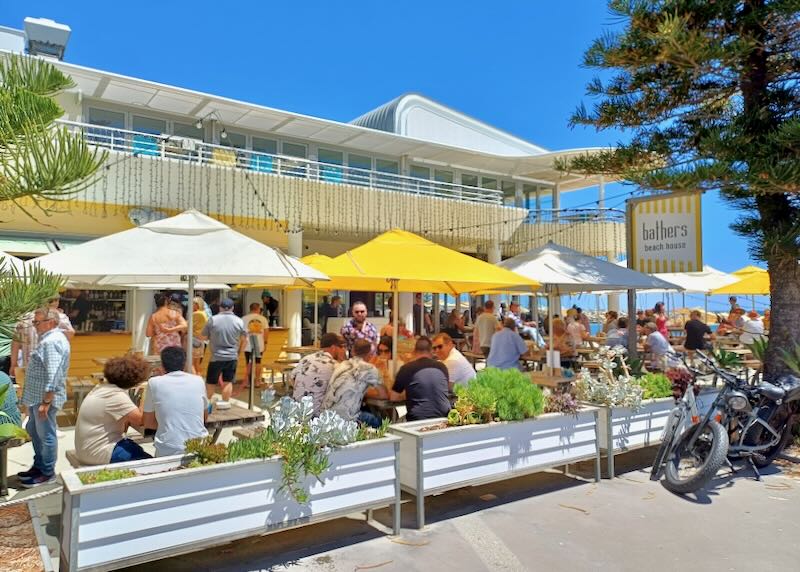 People eat at an outdoor cafe under yellow and white umbrellas.