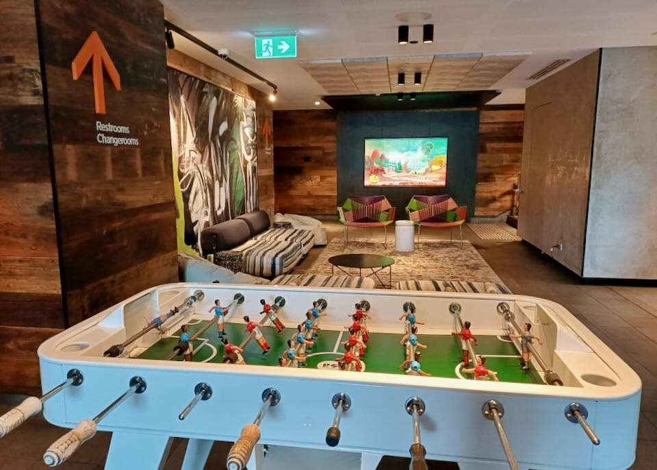 A hotel lobby with large colorful artwork, patchwork chairs, and a foozeball table.