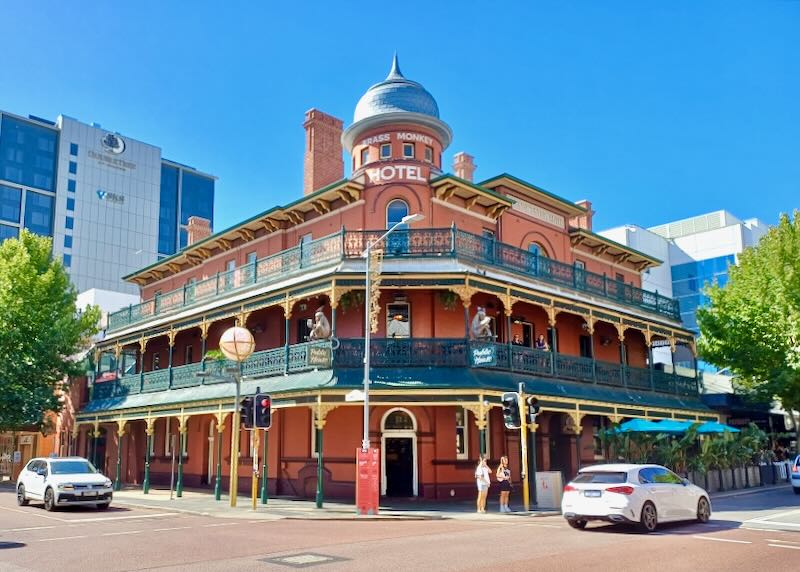 A red brick building with dark green ornate metal railings on the balcony's on the second and third floors.