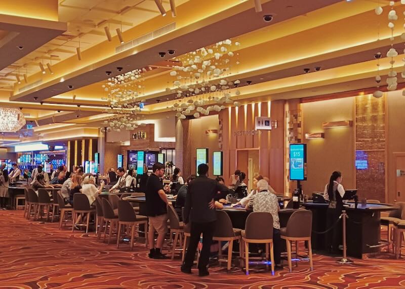 People stand around a black jack table in a casino.