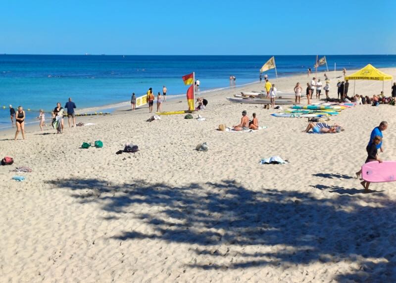 People sit on white sand in the sun and watch the blue ocean.