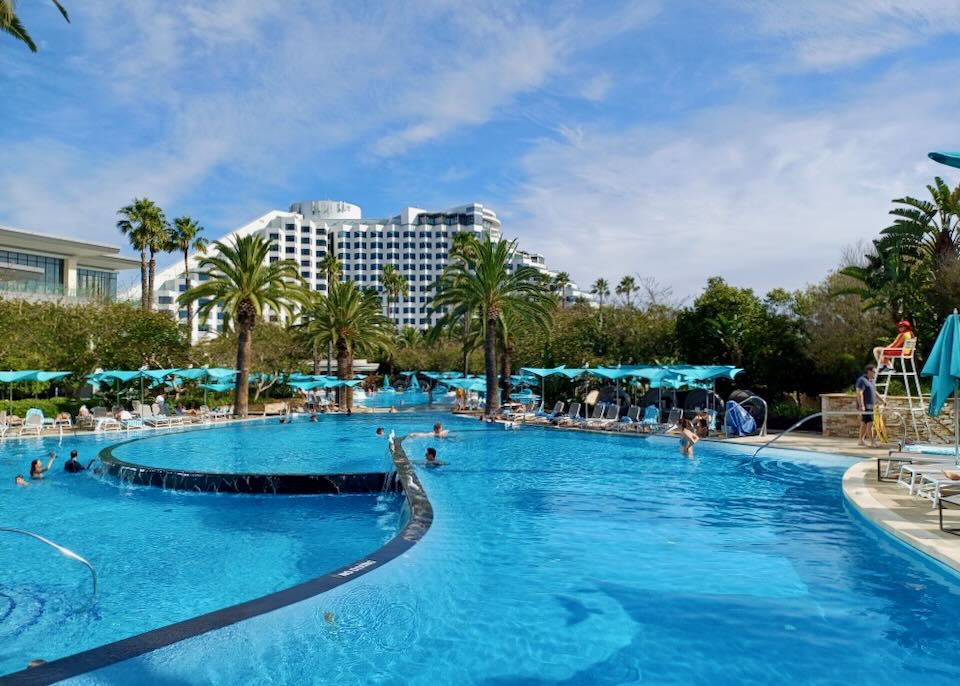 A large multi-level pool with overflow short waterfalls sits in front of a hotel.