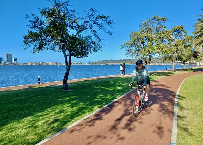 A man rides his bike on an orange path along the water.