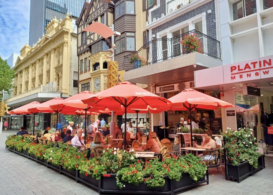 People dine under red umbrellas on and outdoor stone walkway.