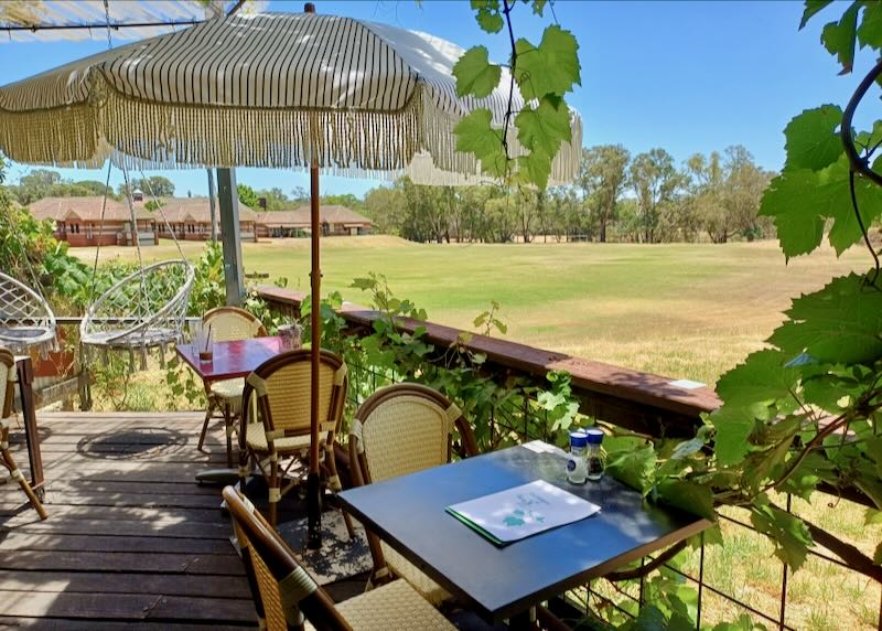 Outdoor tables sit on a deck with umbrellas overlooking a large lawn.