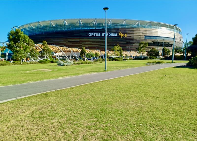 A round enclosed sports stadium sits on a large green lawn.