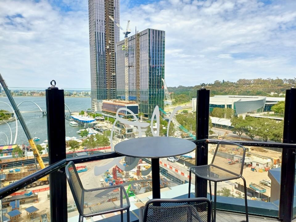 A table sits on a balcony overlooking a water inlet and tall buildings.