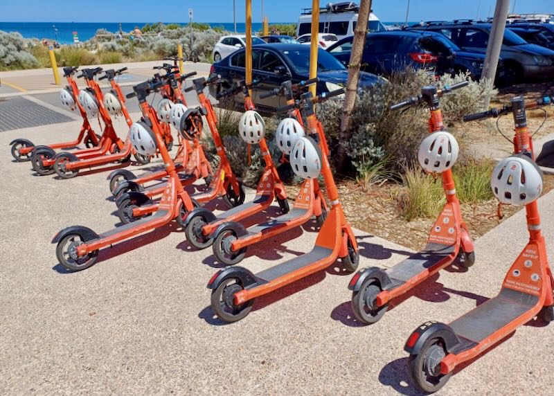 Orange scooters line a sidewalk.