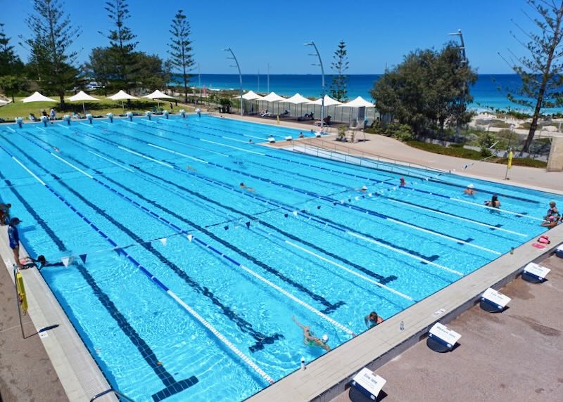 A large long olympic-sized lane pool next to the ocean.