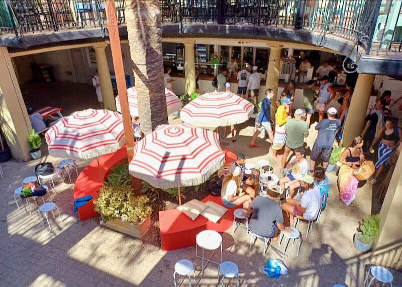 People sit outside enjoying food at tables in a courtyard.