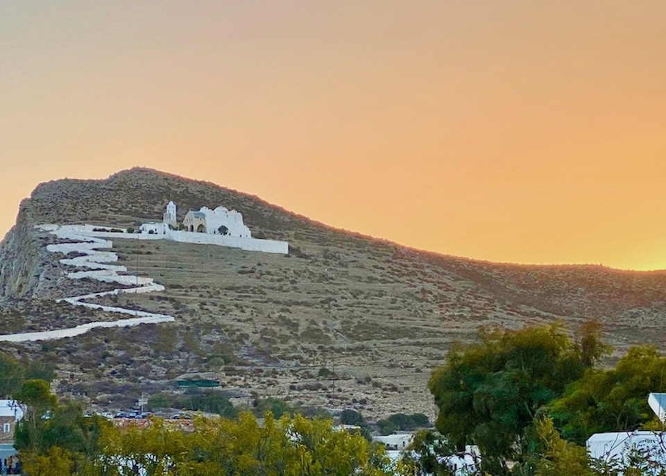 A long zigzagging path leads up a steep hill to a grand, domed church above Chora, Folegandros.