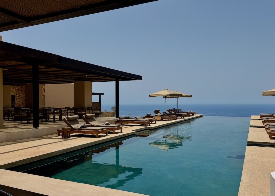 An infinity pool lined with sunbed and umbrella sets next to an open-air restaurant overlooking the sea at Gundari hotel in Folegandros.